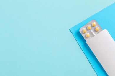 Photo of Blister of contraceptive pills in package on light blue background, top view. Space for text