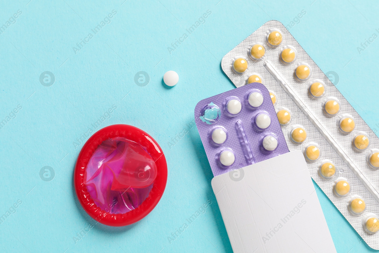 Photo of Blisters of contraceptive pills and condom on light blue background, flat lay