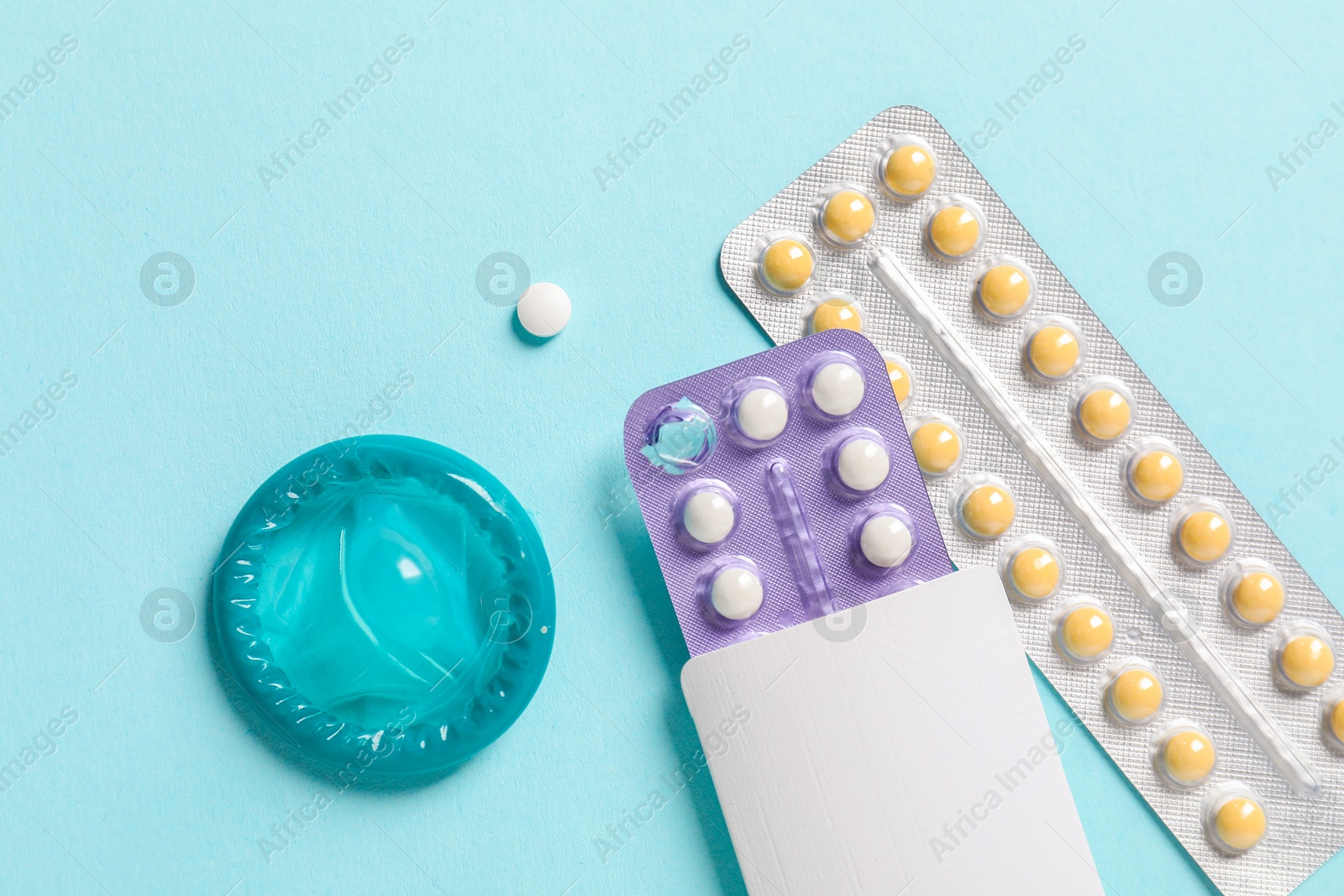 Photo of Blisters of contraceptive pills and condom on light blue background, flat lay