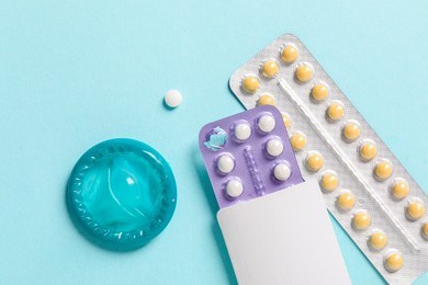 Photo of Blisters of contraceptive pills and condom on light blue background, flat lay