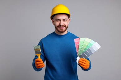 Photo of Man wearing hardhat with paintbrush and color selection chart on light grey background