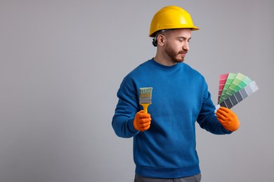 Photo of Man wearing hardhat with paintbrush and color selection chart on light grey background. Space for text