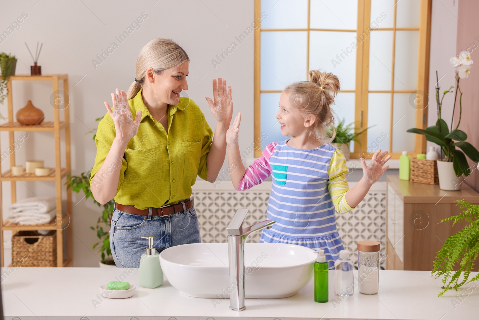 Photo of Happy mother and daughter having fun while washing their hands in bathroom