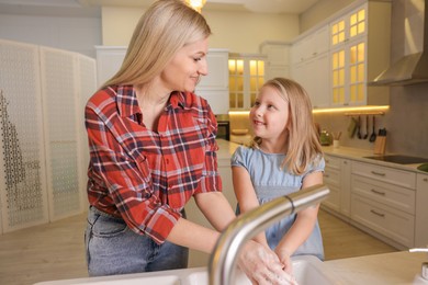 Happy mother and daughter washing their hands in kitchen