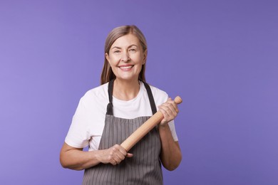 Photo of Happy woman with rolling pin on violet background