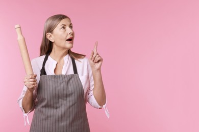 Photo of Woman with rolling pin pointing at something on pink background