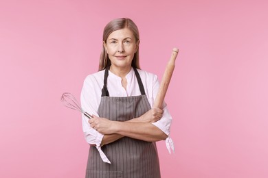 Woman with rolling pin and whisk on pink background