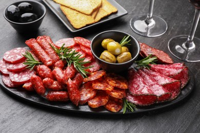 Different smoked sausages, olives, crispbreads and rosemary on black table, closeup