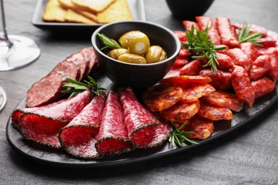 Photo of Different smoked sausages, olives and rosemary on black table, closeup