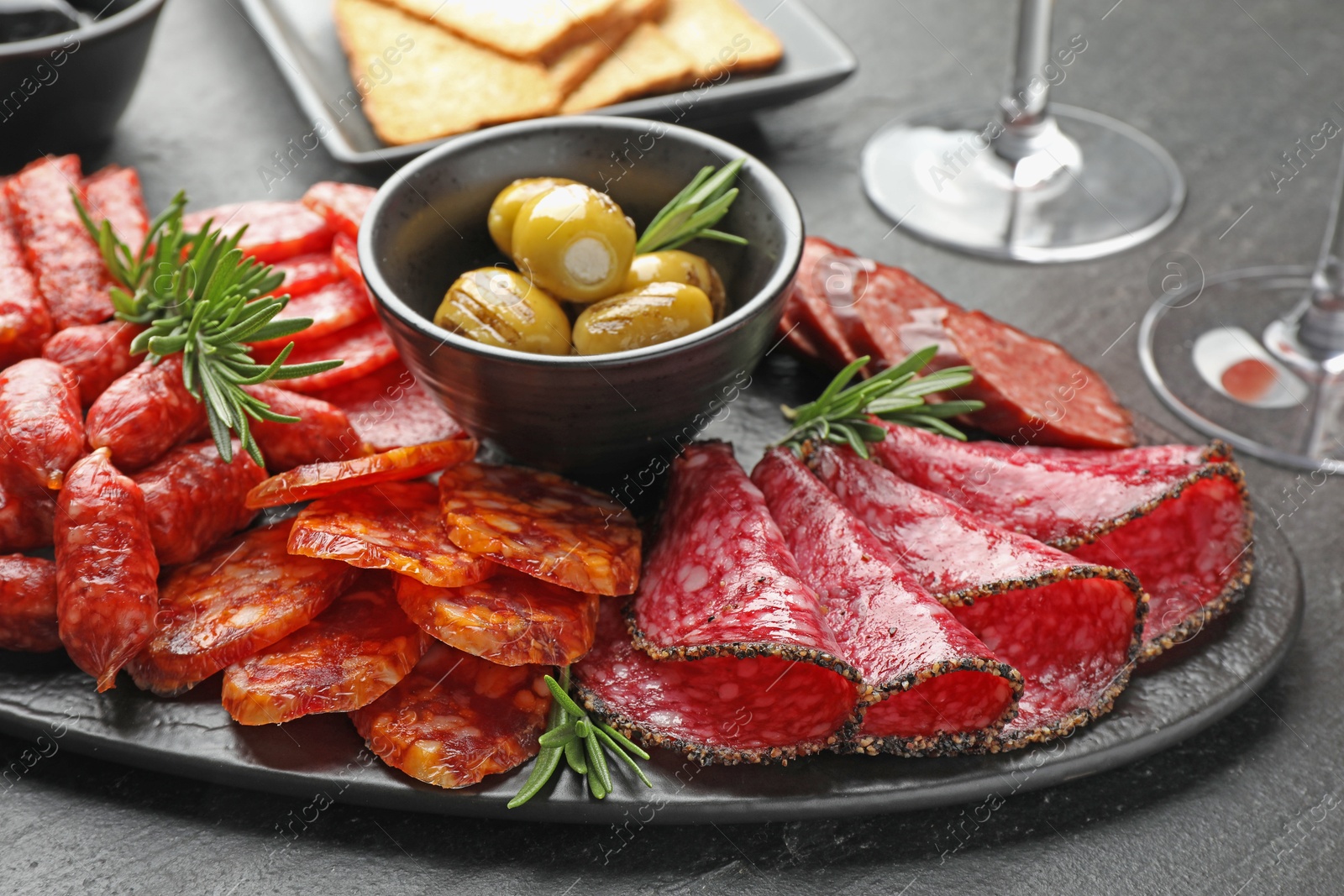 Photo of Different smoked sausages, olives and rosemary on black table, closeup