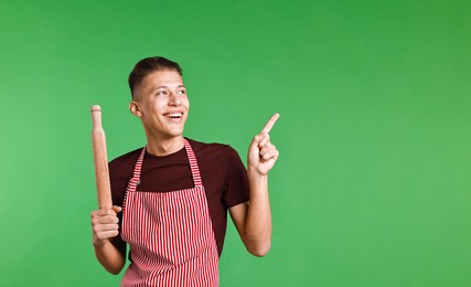 Happy man with rolling pin pointing at something on green background