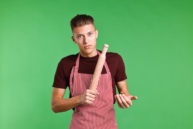 Angry man with rolling pin on green background