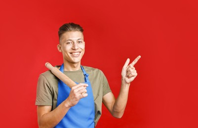 Happy man with rolling pin pointing at something on red background