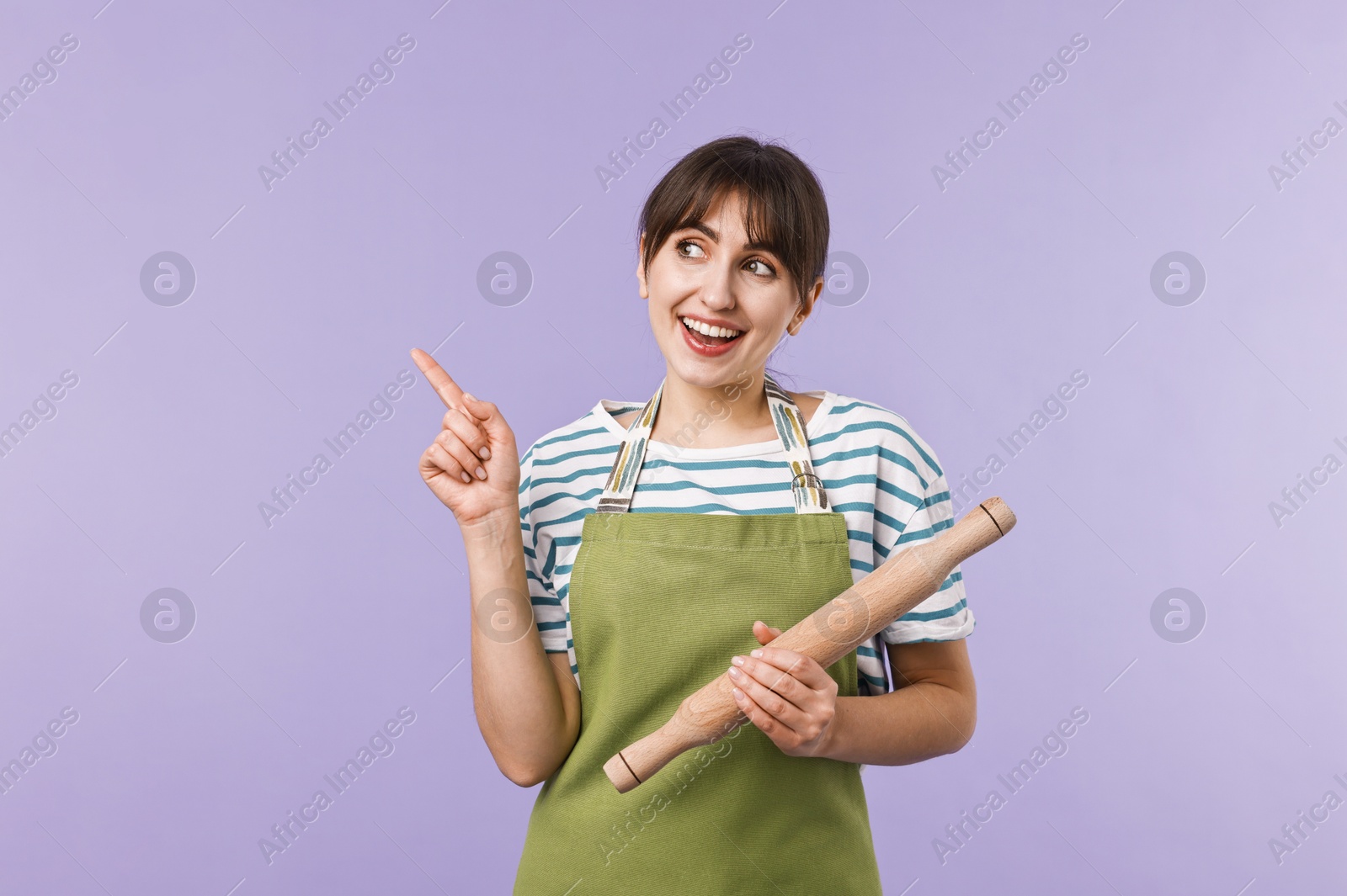 Photo of Woman with rolling pin pointing at something on violet background