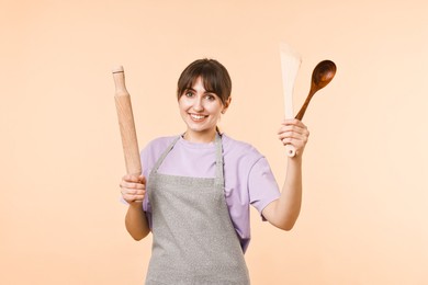 Photo of Happy woman with rolling pin, turner and spoon on beige background