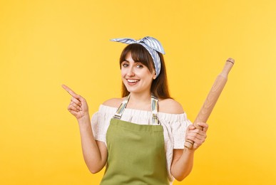 Photo of Woman with rolling pin pointing at something on yellow background