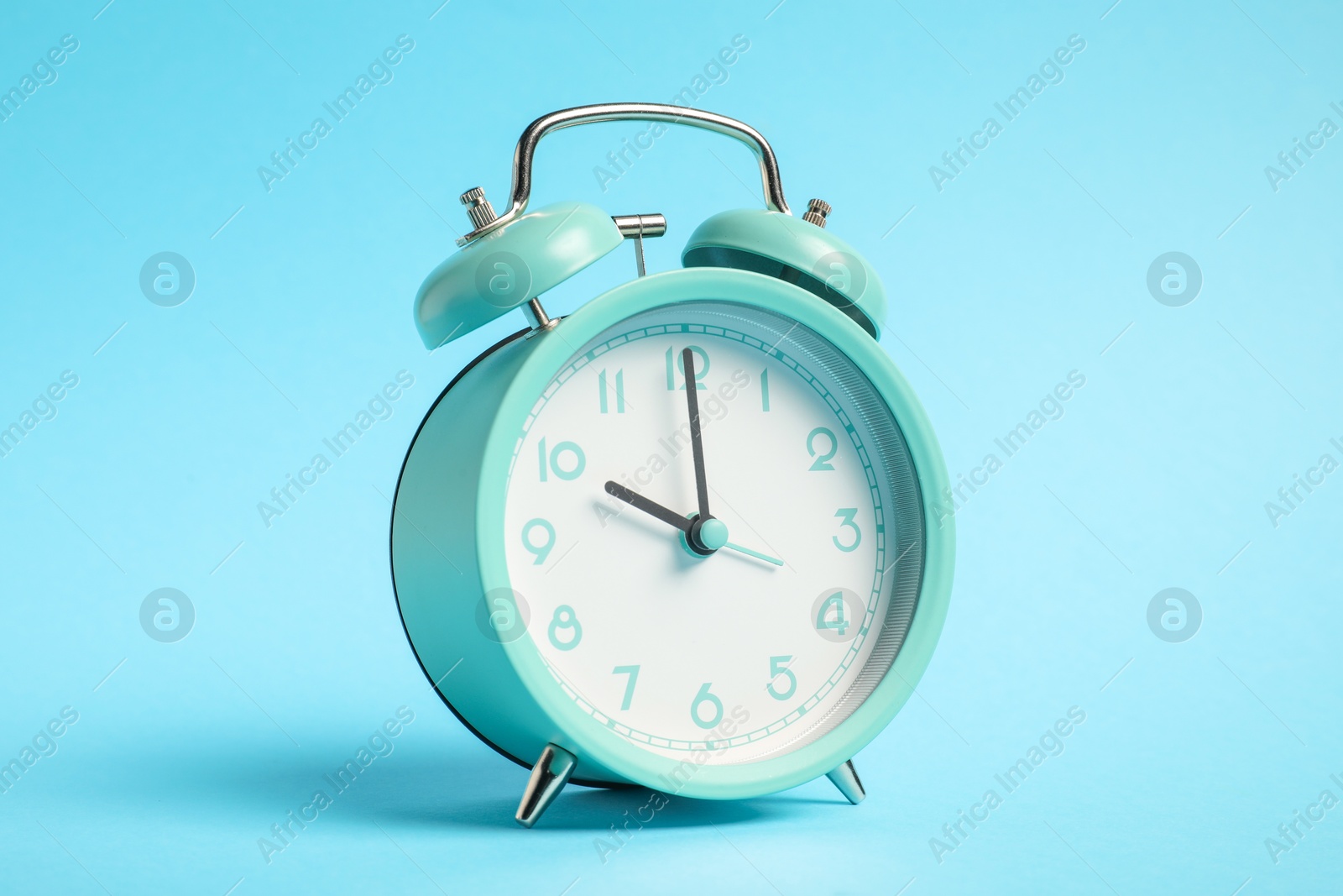Photo of One turquoise alarm clock on light blue background