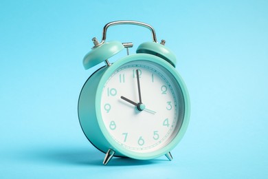 Photo of One turquoise alarm clock on light blue background