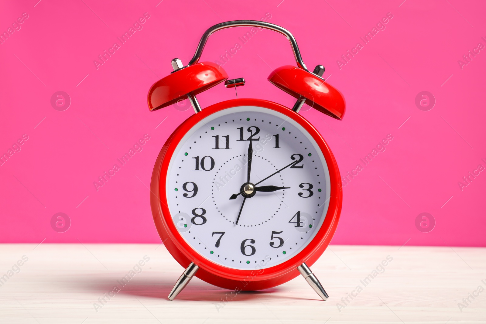 Photo of One red alarm clock on white wooden table against bright pink background