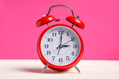 Photo of One red alarm clock on white wooden table against bright pink background