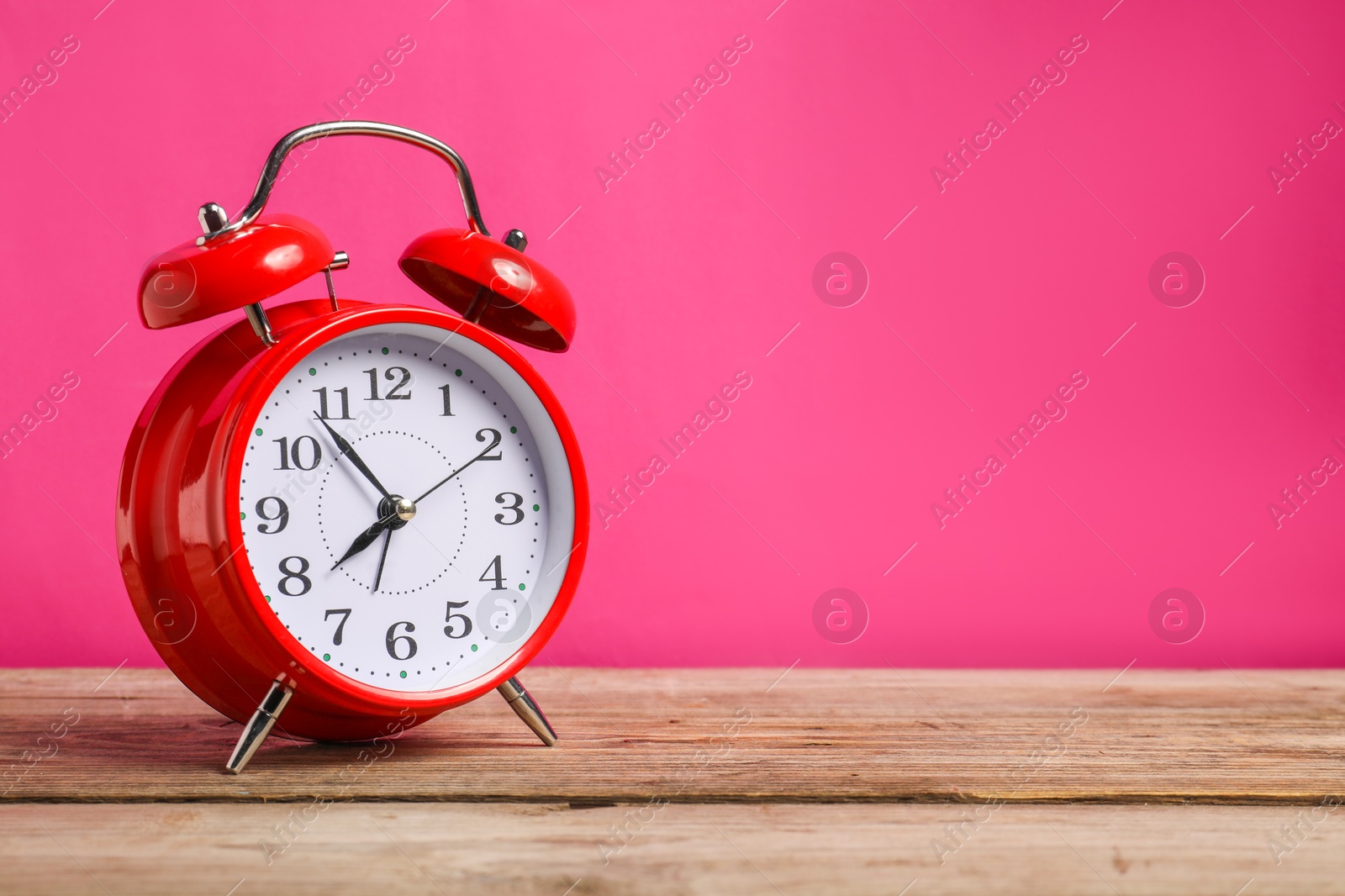 Photo of One red alarm clock on wooden table against bright pink background, space for text