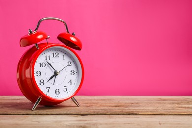 Photo of One red alarm clock on wooden table against bright pink background, space for text