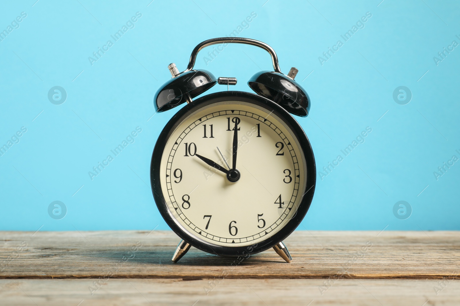 Photo of One black alarm clock on wooden table against light blue background