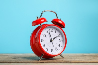 Photo of One red alarm clock on wooden table against light blue background