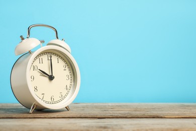 Photo of One white alarm clock on wooden table against light blue background, space for text