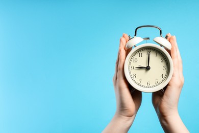 Photo of Woman with white alarm clock on light blue background, closeup. Space for text