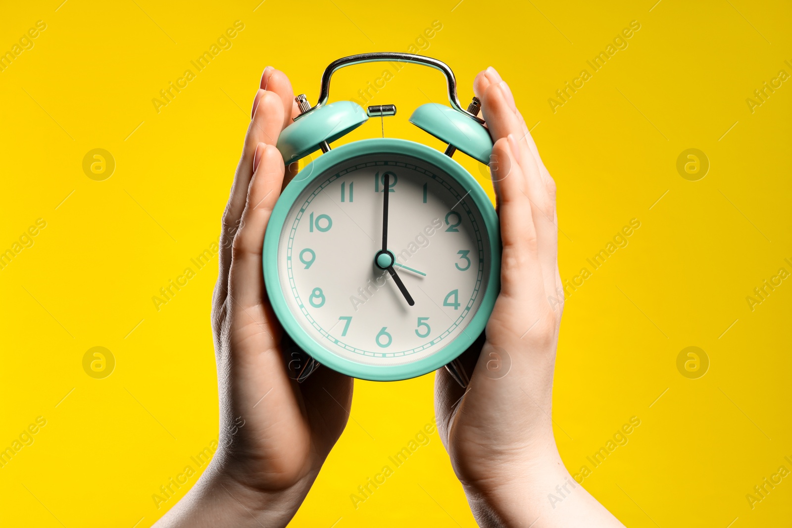 Photo of Woman with turquoise alarm clock on yellow background, closeup