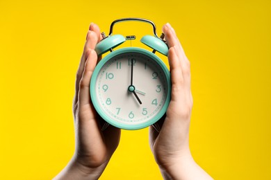 Photo of Woman with turquoise alarm clock on yellow background, closeup