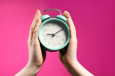 Photo of Woman with turquoise alarm clock on bright pink background, closeup