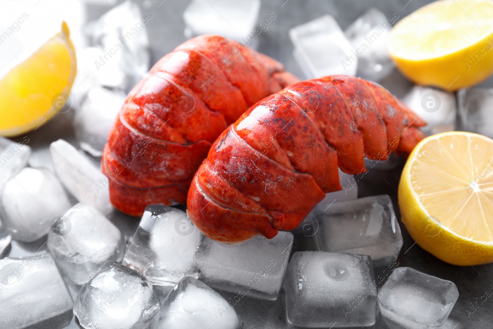 Photo of Tails of boiled lobsters with ice cubes and lemon pieces on grey table, closeup