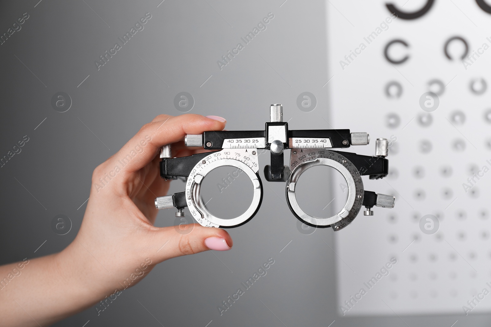 Photo of Woman holding trial frame against vision test chart on gray background, closeup