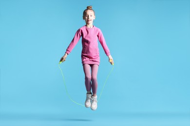 Photo of Cute little girl with jump rope on light blue background