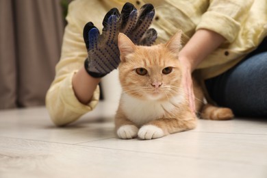 Woman brushing cat's hair with glove on floor at home, closeup. Pet grooming