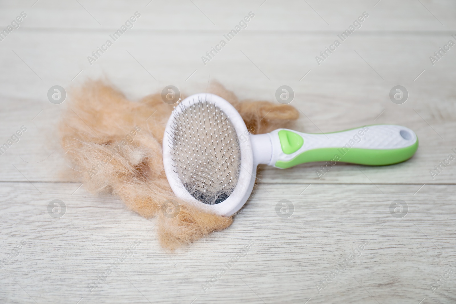 Photo of Grooming brush and pile of pet's hair on wooden floor, closeup