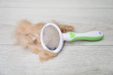 Photo of Grooming brush and pile of pet's hair on wooden floor, closeup