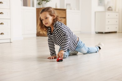 Little girl playing with toy car on floor at home