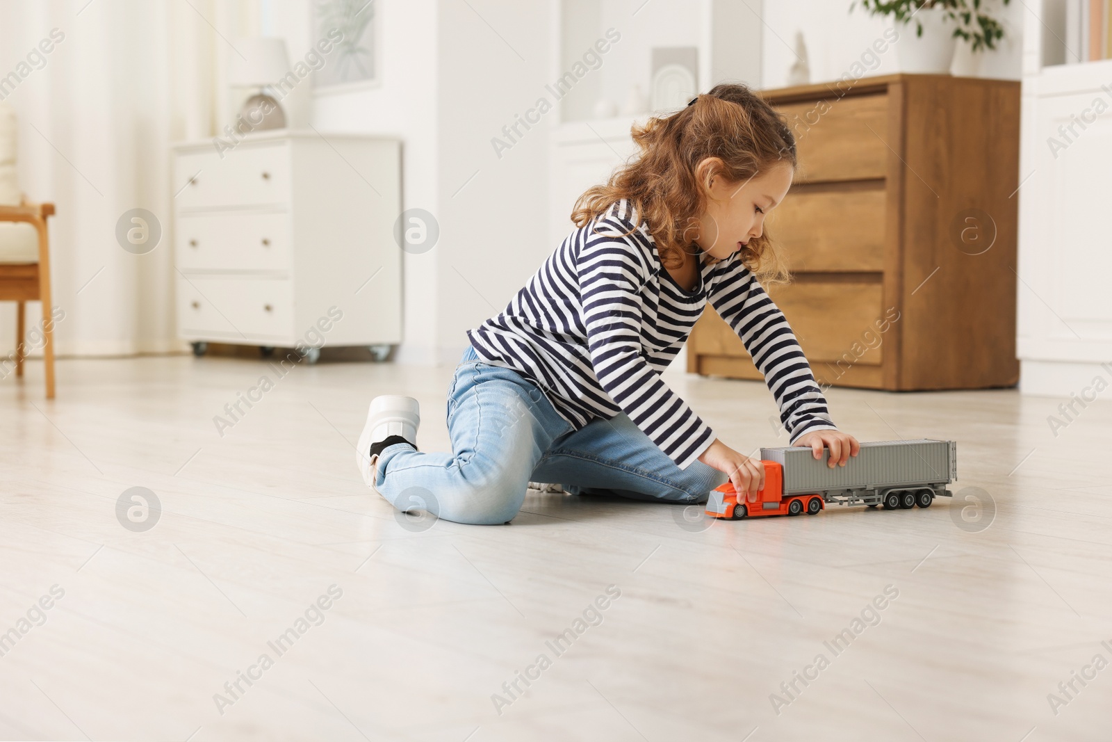 Photo of Little girl playing with toy car on floor at home