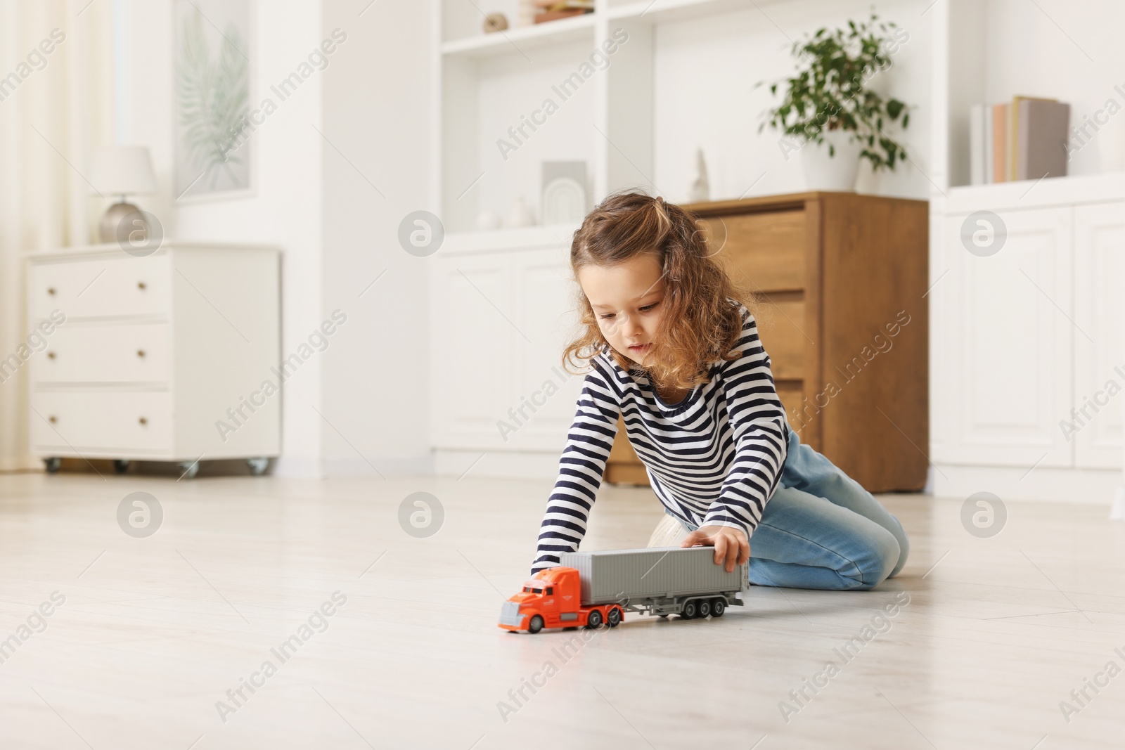 Photo of Little girl playing with toy car on floor at home, space for text