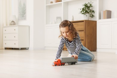 Little girl playing with toy car on floor at home, space for text