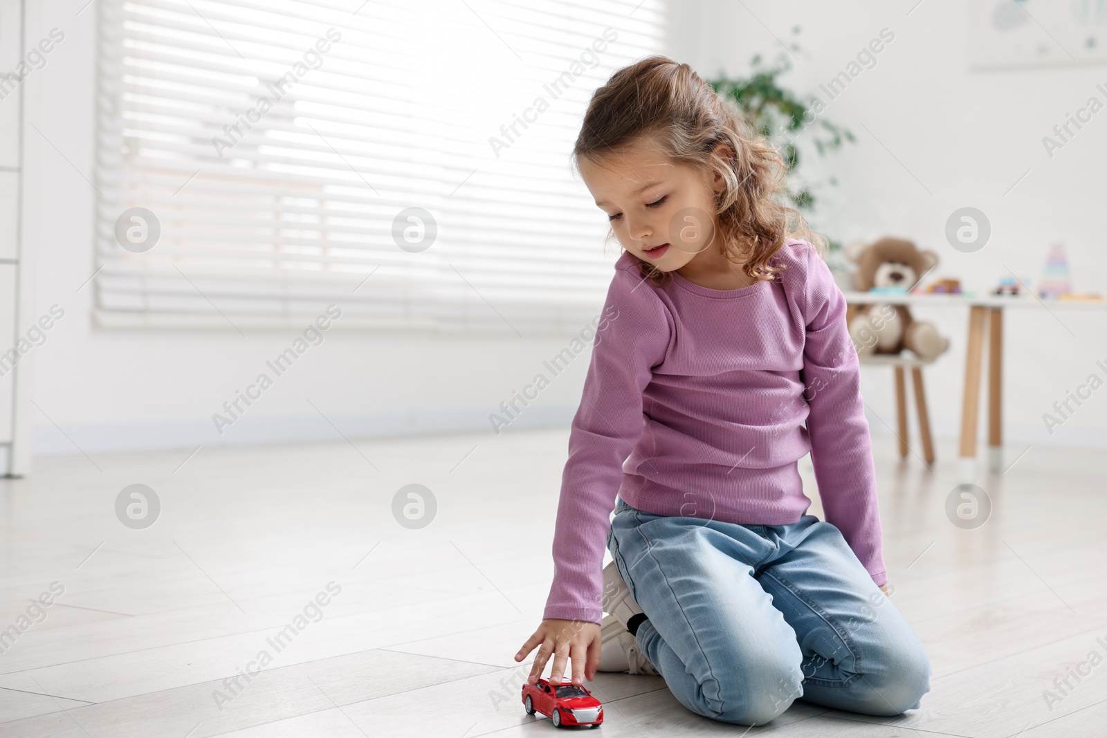 Photo of Little girl playing with toy car on floor at home, space for text