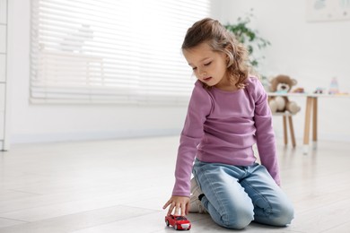 Little girl playing with toy car on floor at home, space for text