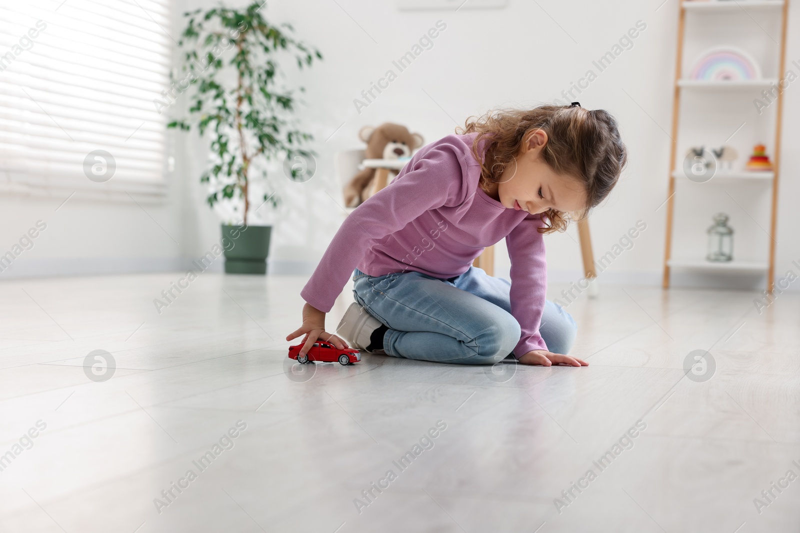 Photo of Little girl playing with toy car on floor at home, space for text