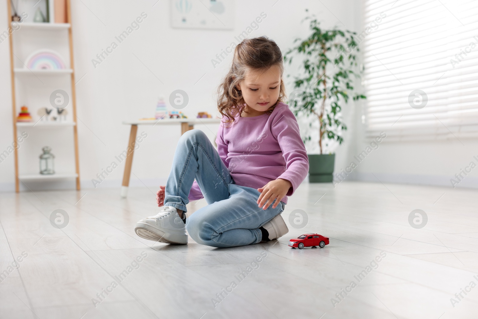 Photo of Little girl playing with toy car on floor at home