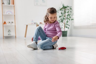 Little girl playing with toy car on floor at home