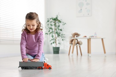 Photo of Little girl playing with toy car on floor at home, space for text