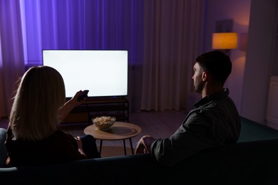 Lovely couple watching tv at home in evening, back view